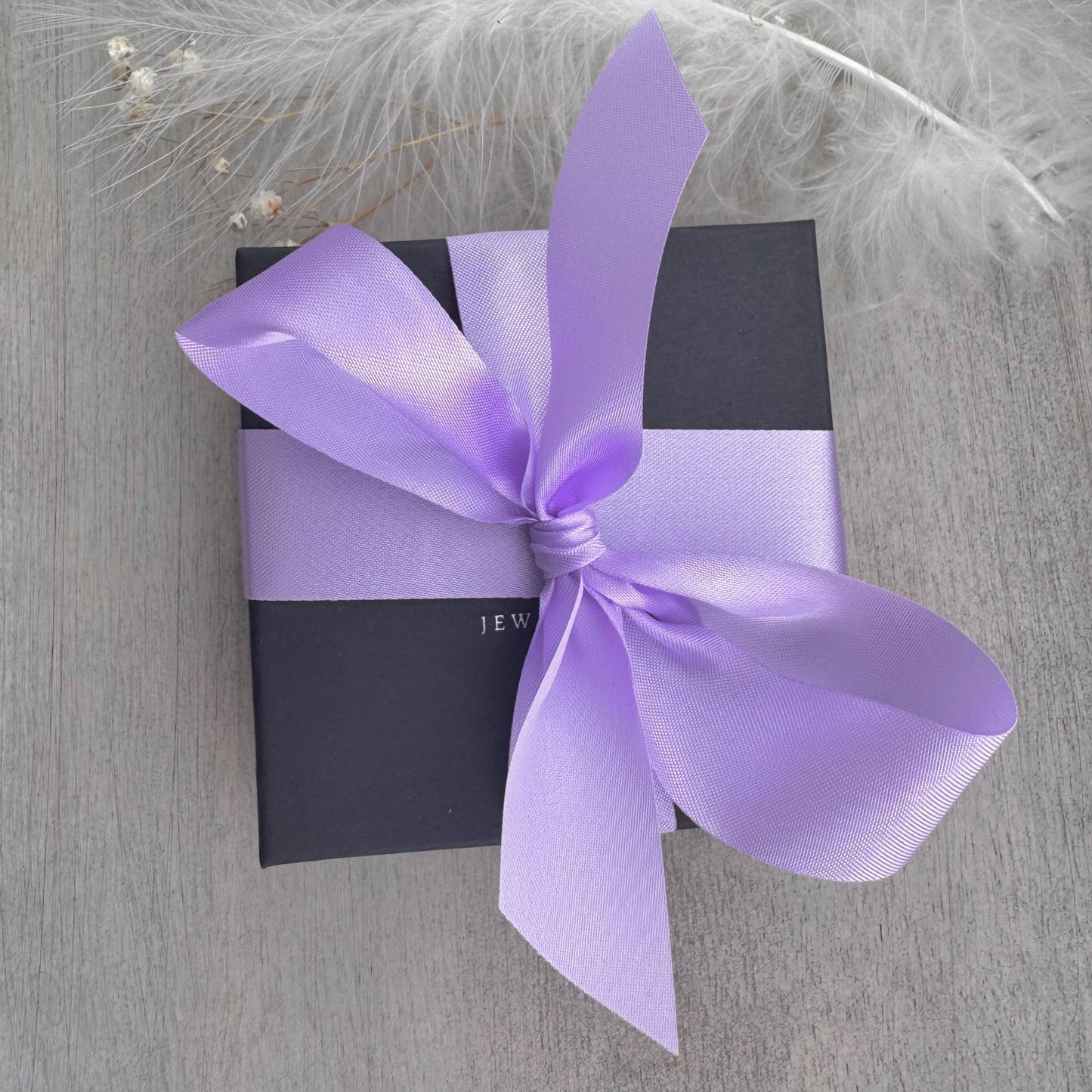 A gift box with a purple ribbon tied around it, placed on a wooden surface.
