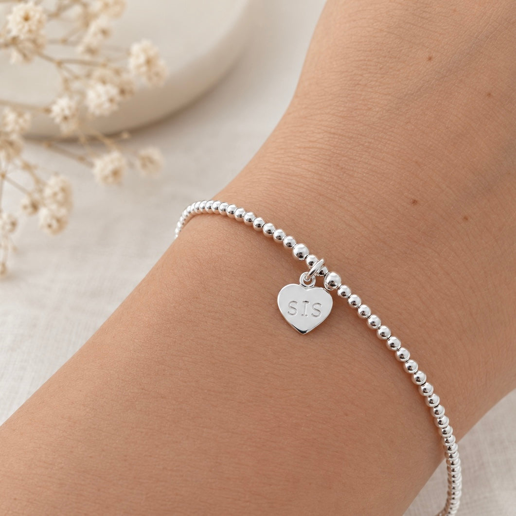 A silver bracelet with a heart-shaped charm attached, resting on a person's wrist.