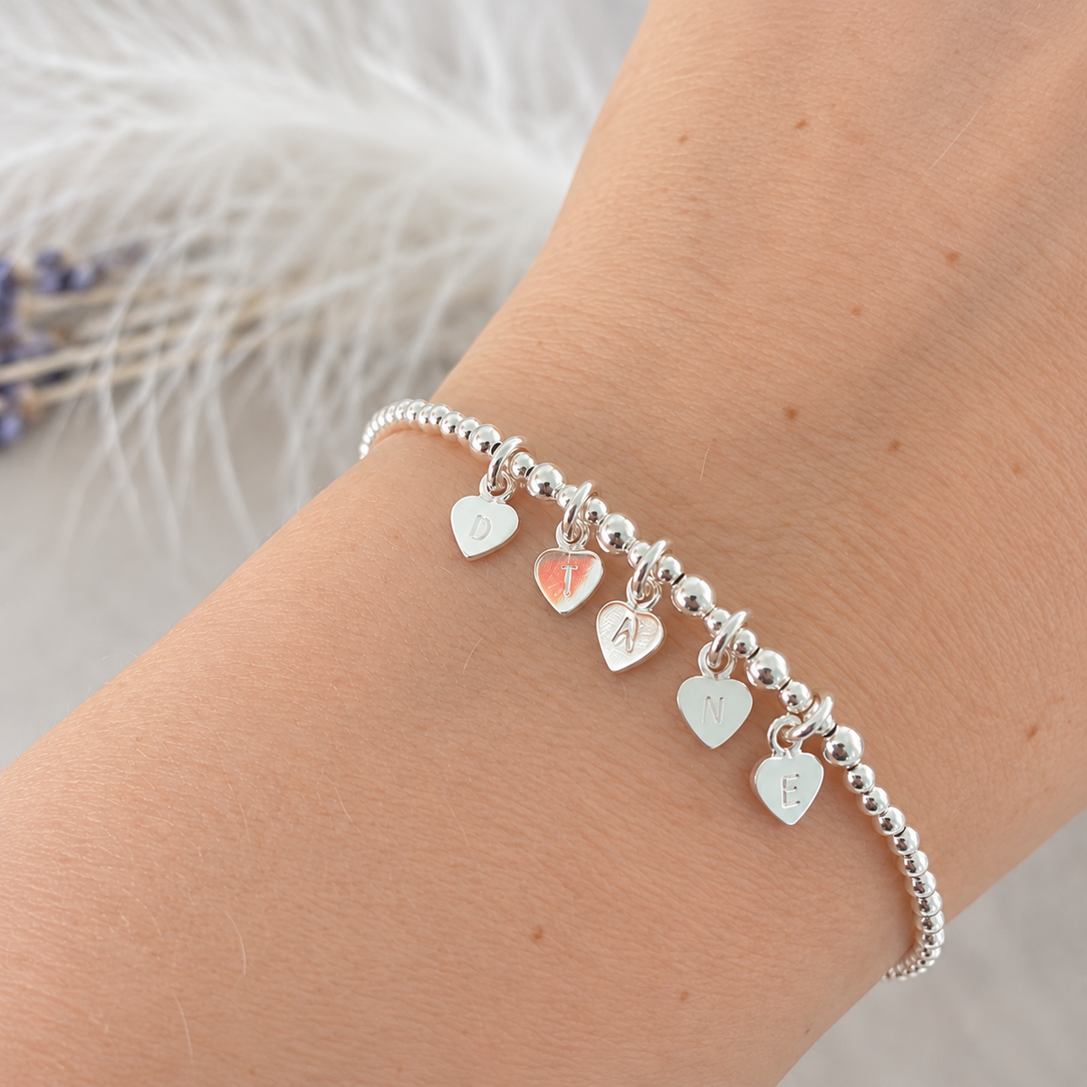 A silver bracelet with heart-shaped charms on a person's wrist.