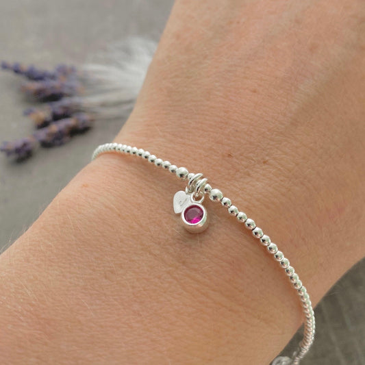 A silver bracelet with a charm and a small red gemstone is worn on a person's wrist.