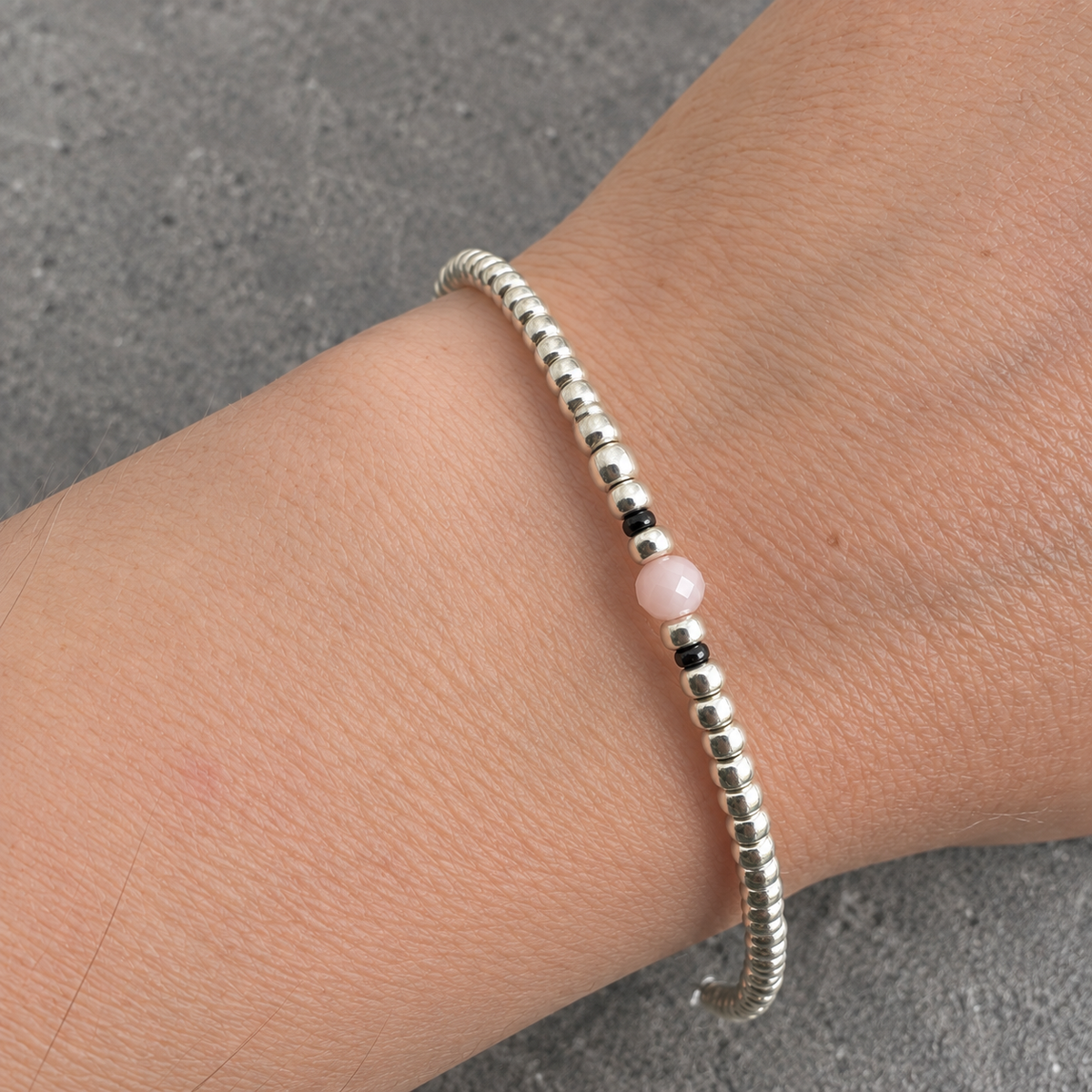 A silver bracelet with a single pink bead is worn on a person's wrist.
