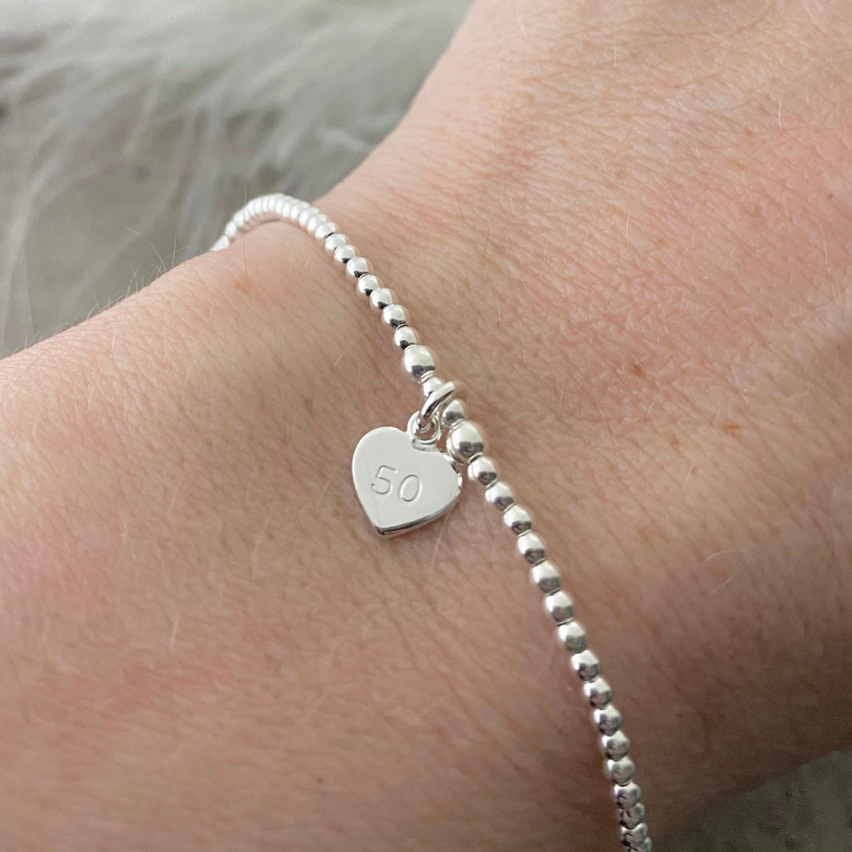A silver bracelet with a heart-shaped charm attached, displaying the number "50" on it.