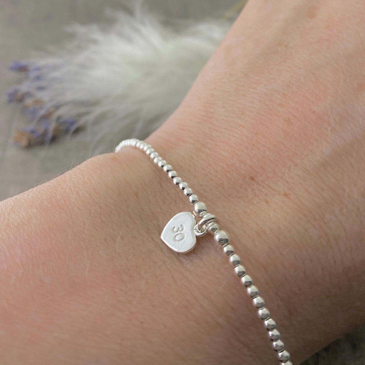 A silver bracelet with a heart-shaped charm attached, and the charm displays the number "30".
