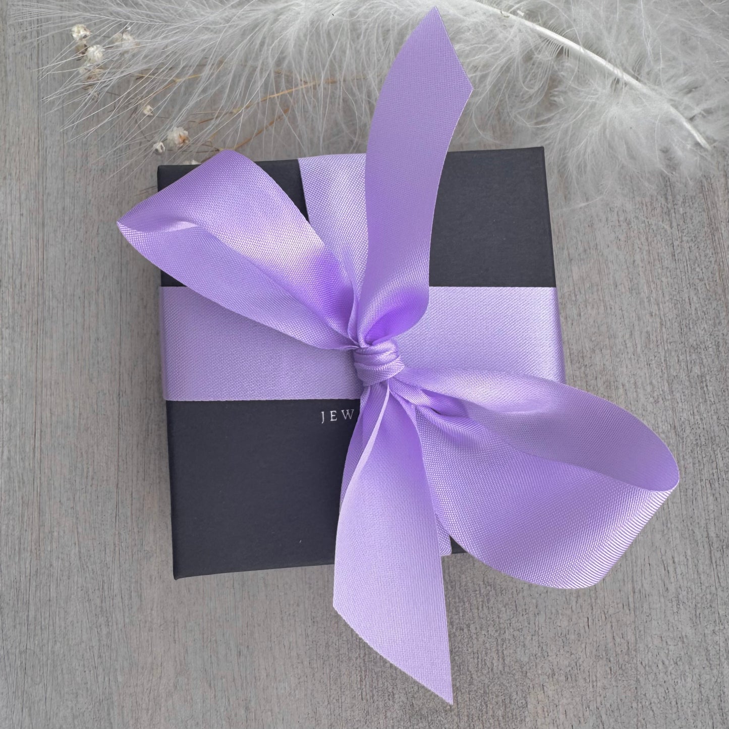 A gift box with a purple ribbon tied around it, placed on a wooden surface.