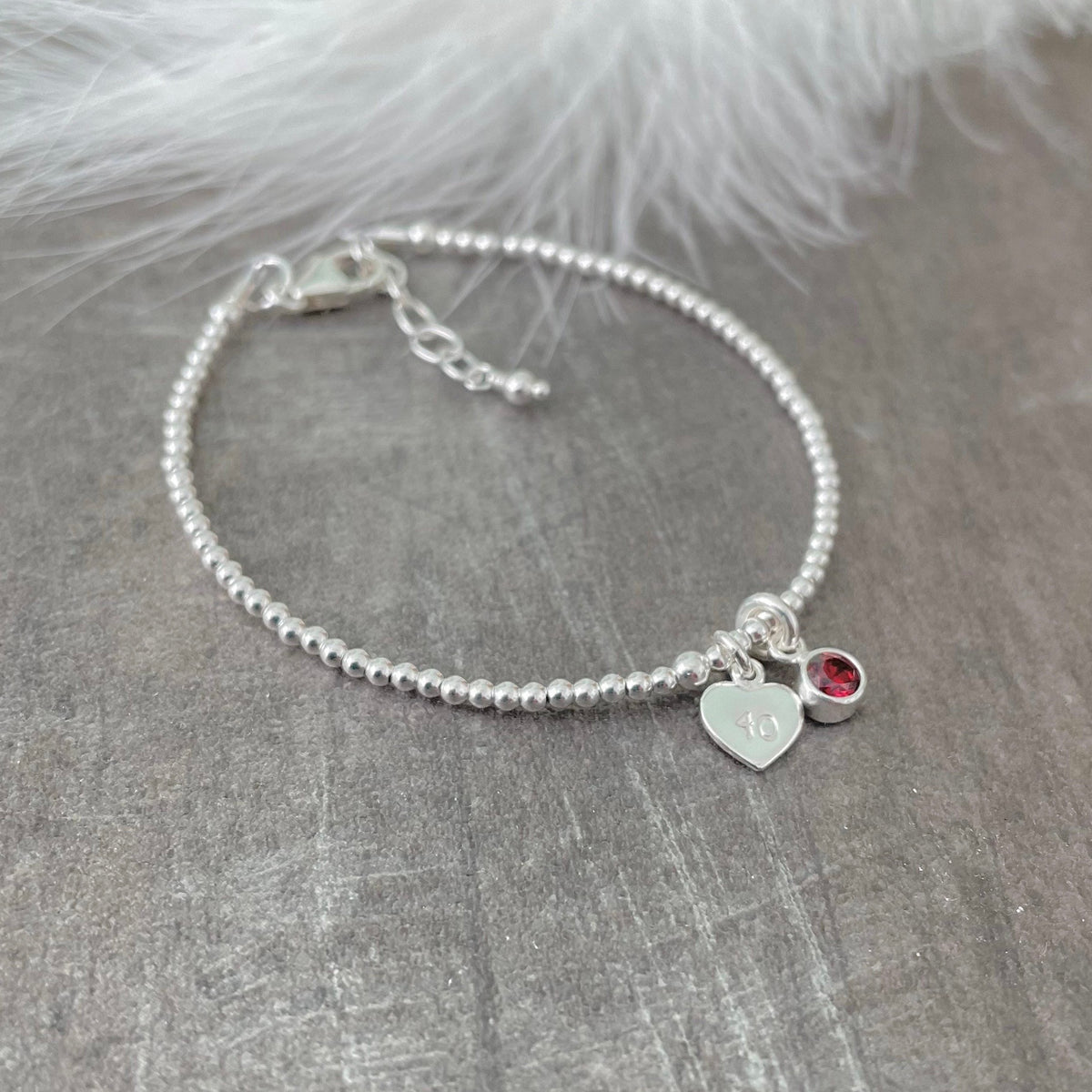 A silver bracelet with a charm and a red gemstone is displayed on a grey surface.