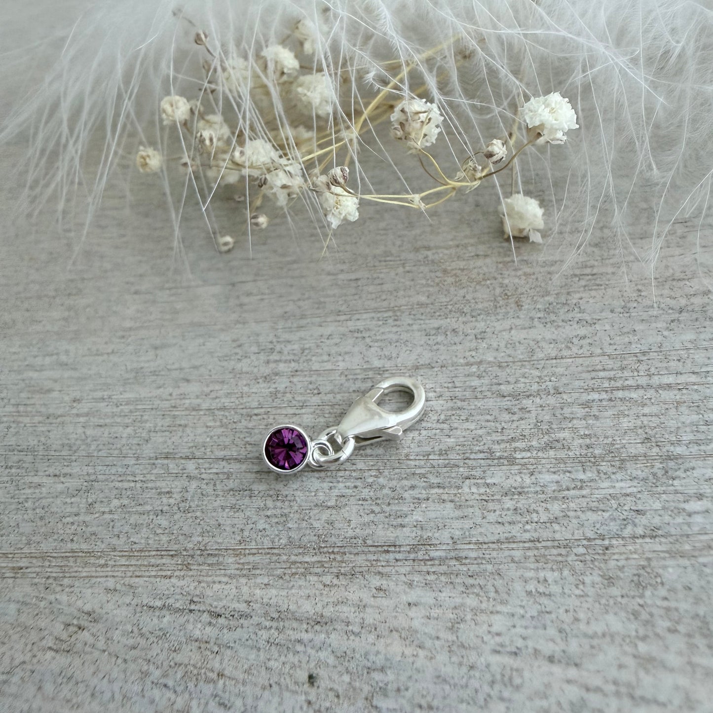 Silver charm with a purple gemstone on a textured surface