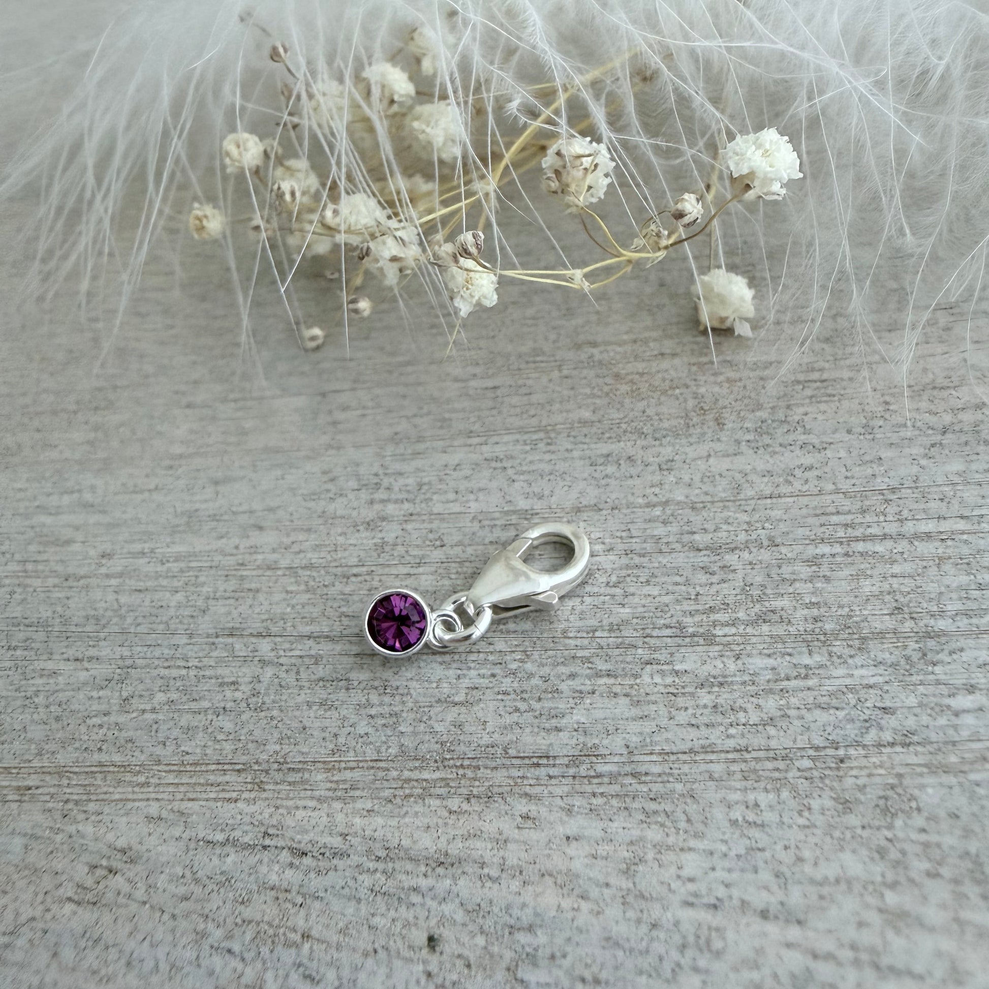 Silver charm with a purple gemstone on a textured surface
