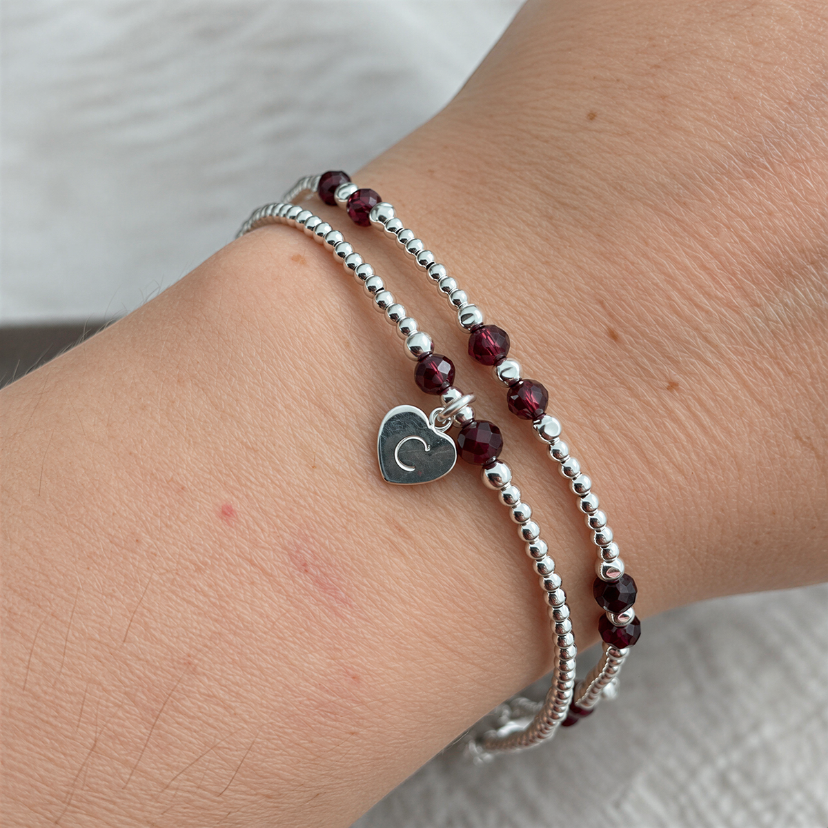 A silver bracelet with red gemstone beads and a heart-shaped charm on the wrist.