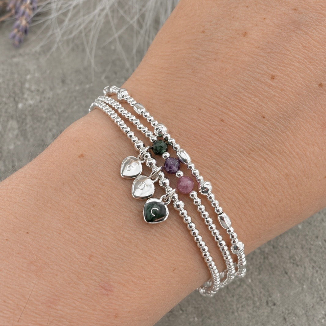 A silver bracelet with three charms on it, each with a letter on it, is worn on a person's wrist.