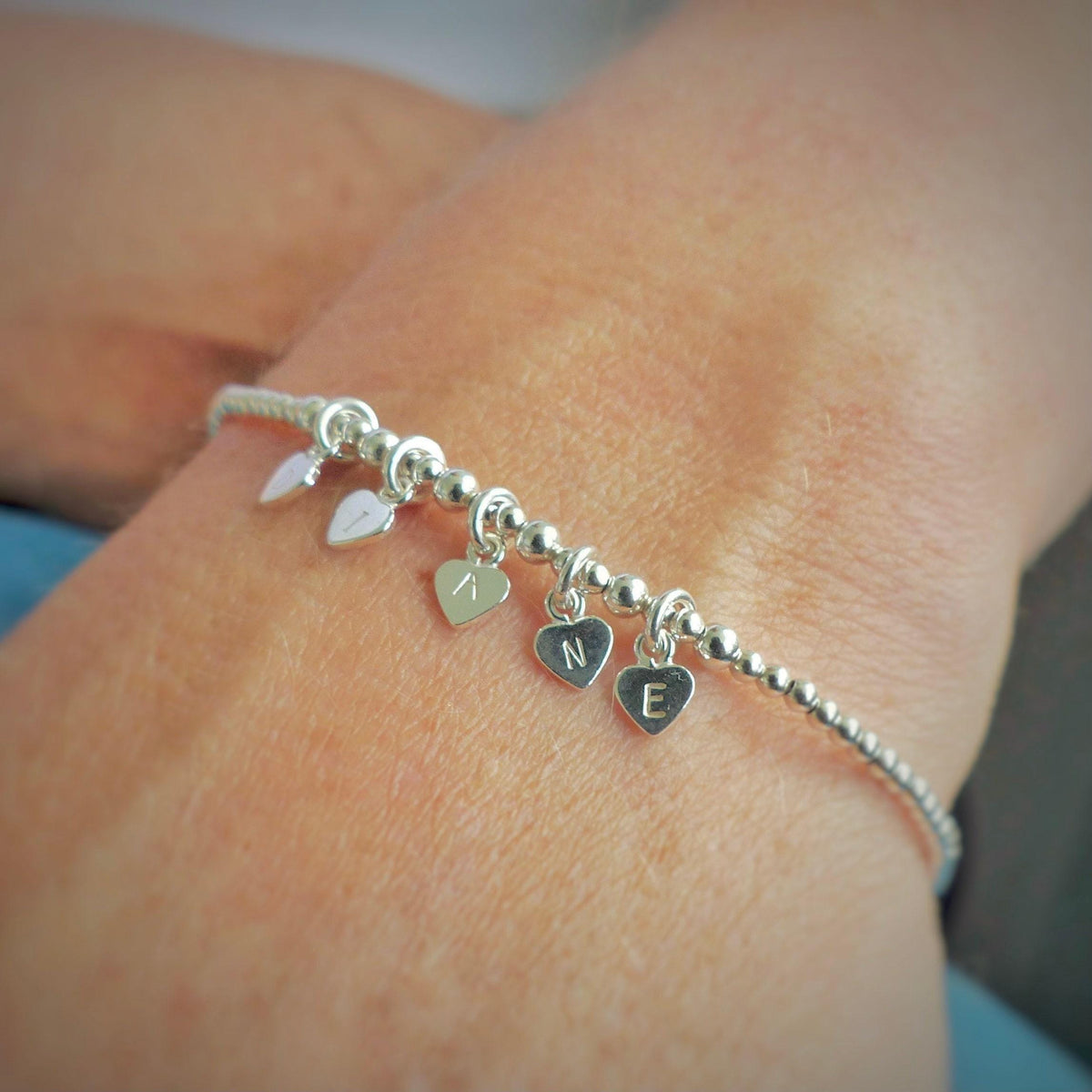 A silver bracelet with heart-shaped charms on it, each containing a letter of the alphabet.