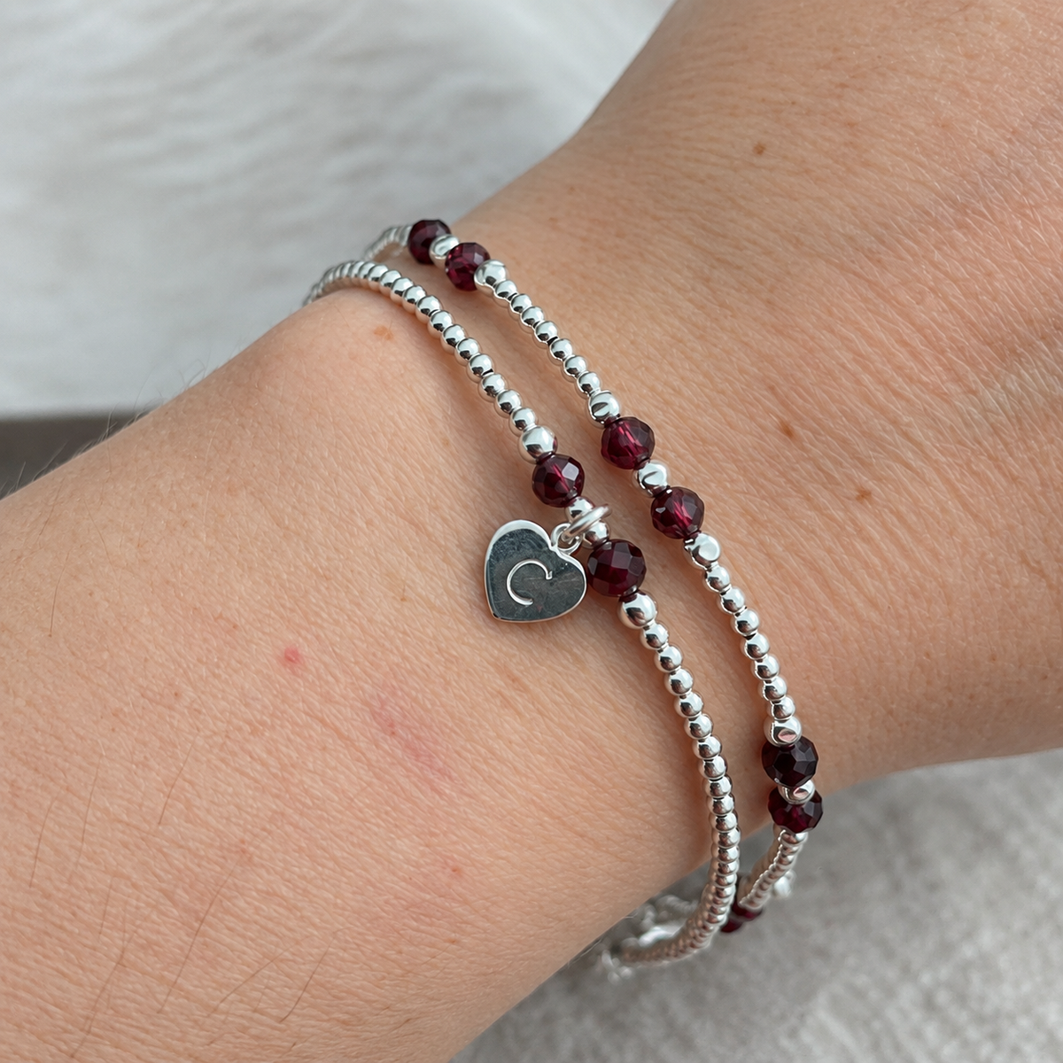 A silver bracelet with red gemstone beads and a heart-shaped charm on the wrist.